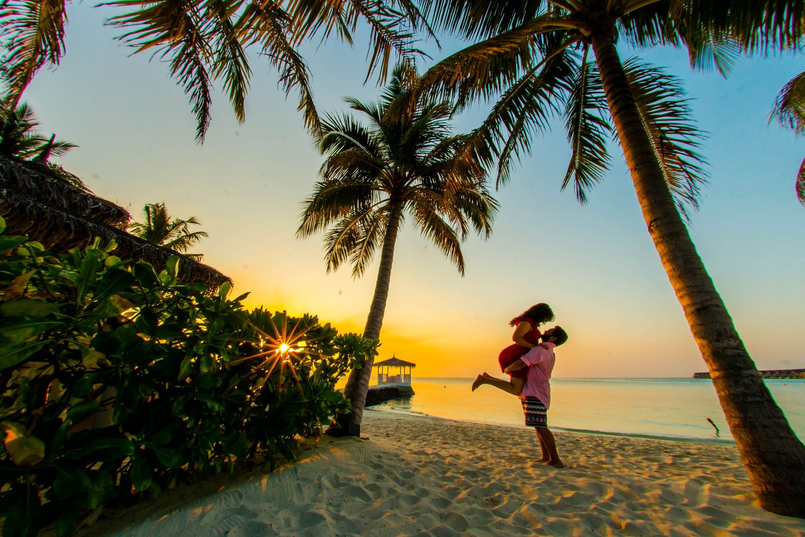 A romantic couple enjoying sunset on a Maldives beach surrounded by palm trees and ocean views.