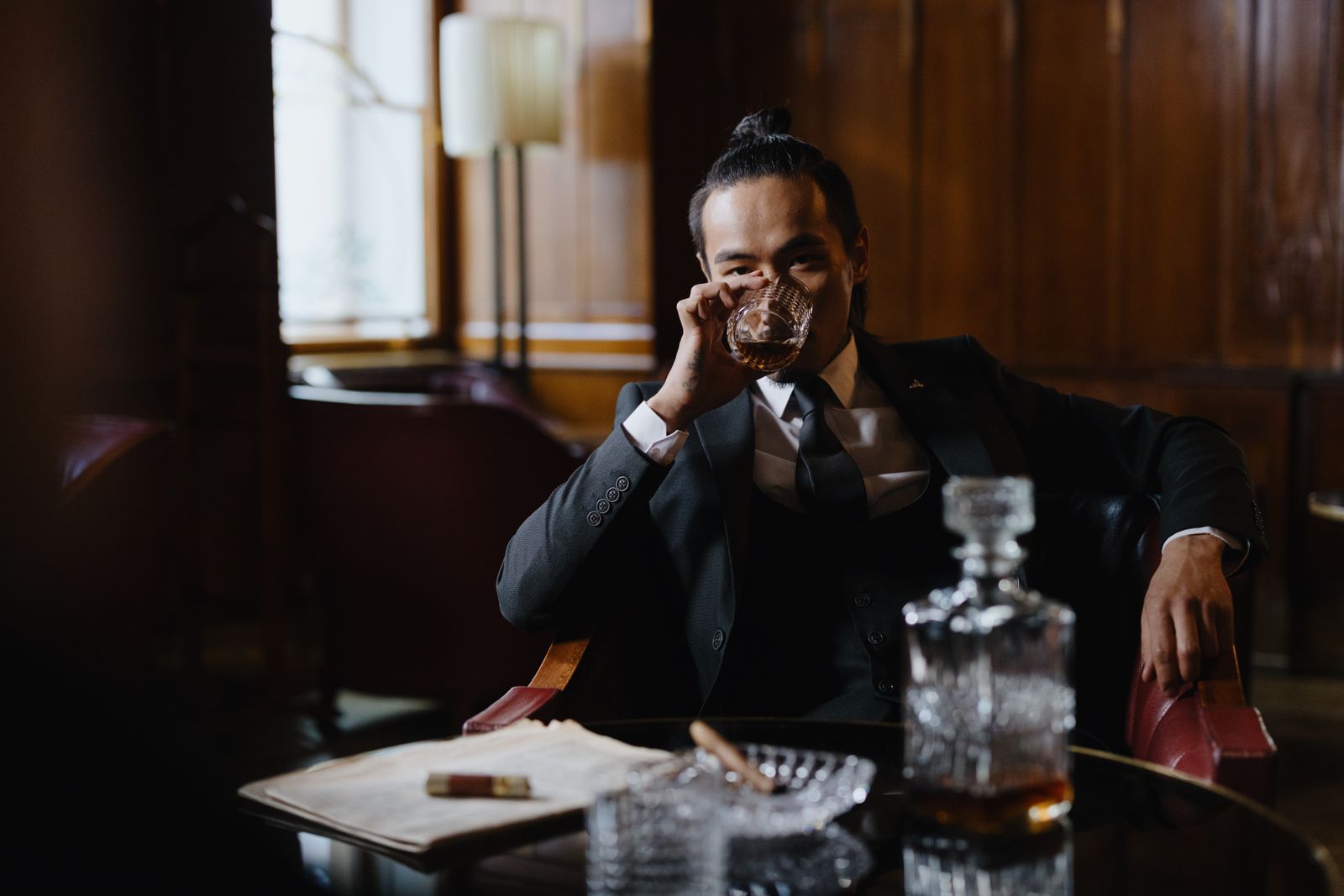 A sophisticated man in a suit savoring a glass of whiskey in an upscale room.
