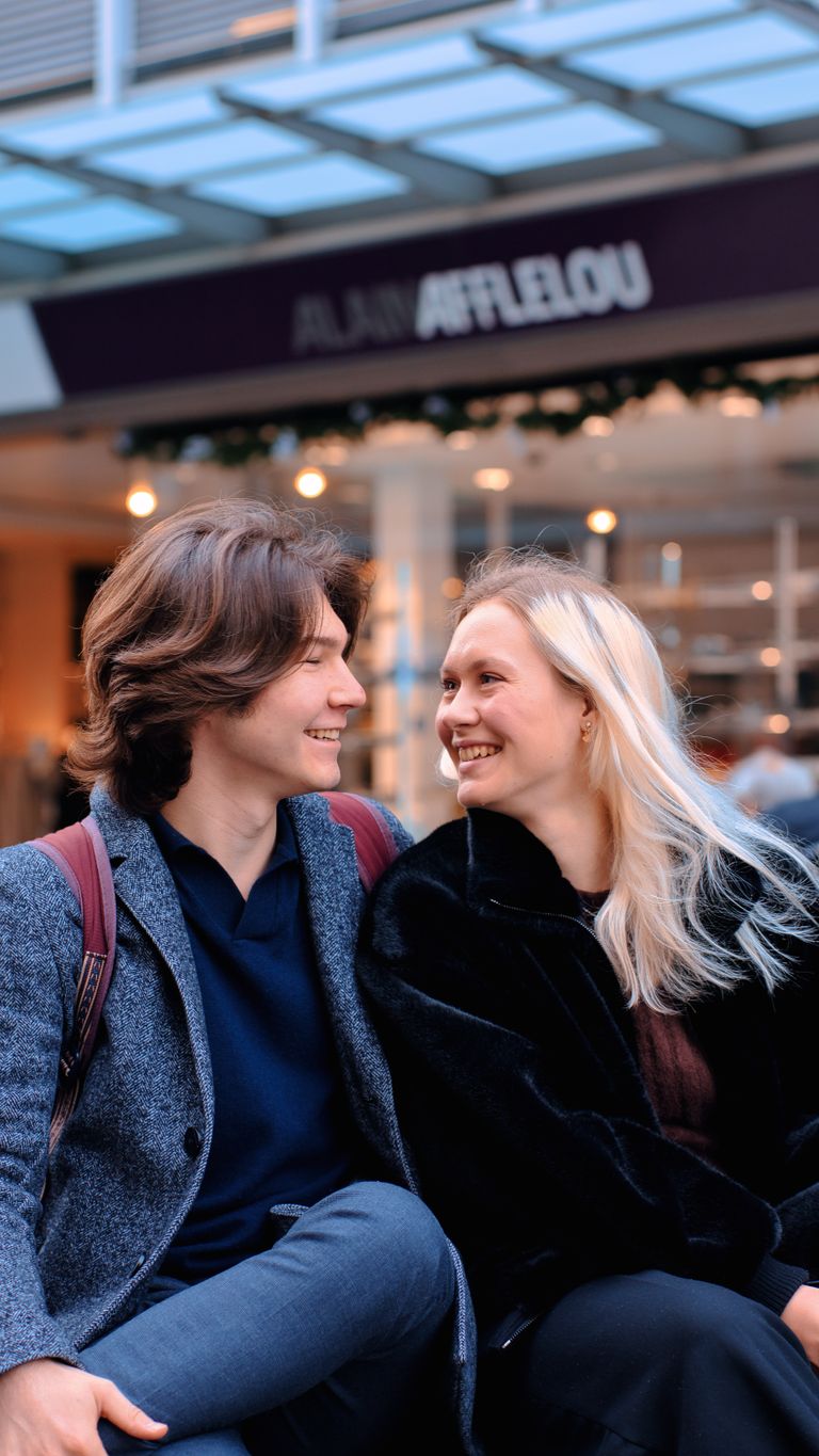 A cheerful young couple smiling at each other in a vibrant urban location, enjoying a moment together.