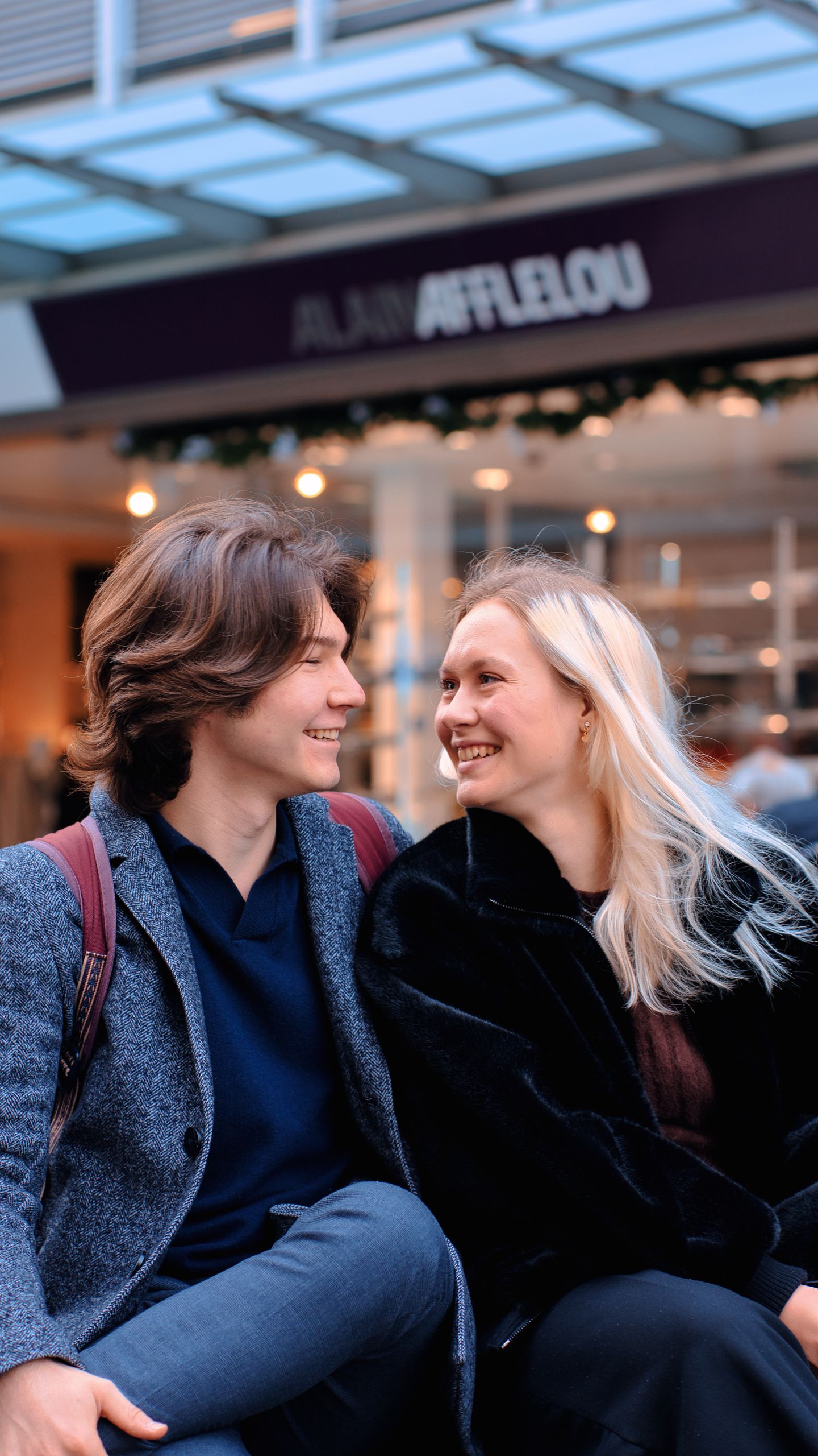 A cheerful young couple smiling at each other in a vibrant urban location, enjoying a moment together.