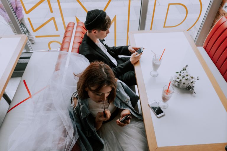 A couple in wedding attire enjoys milkshakes at a café, capturing a blend of tradition and modern life.