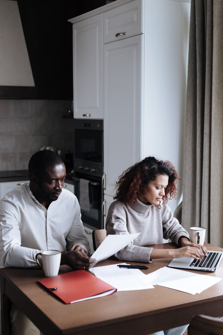 A couple reviewing documents together on a laptop in a modern kitchen setting.