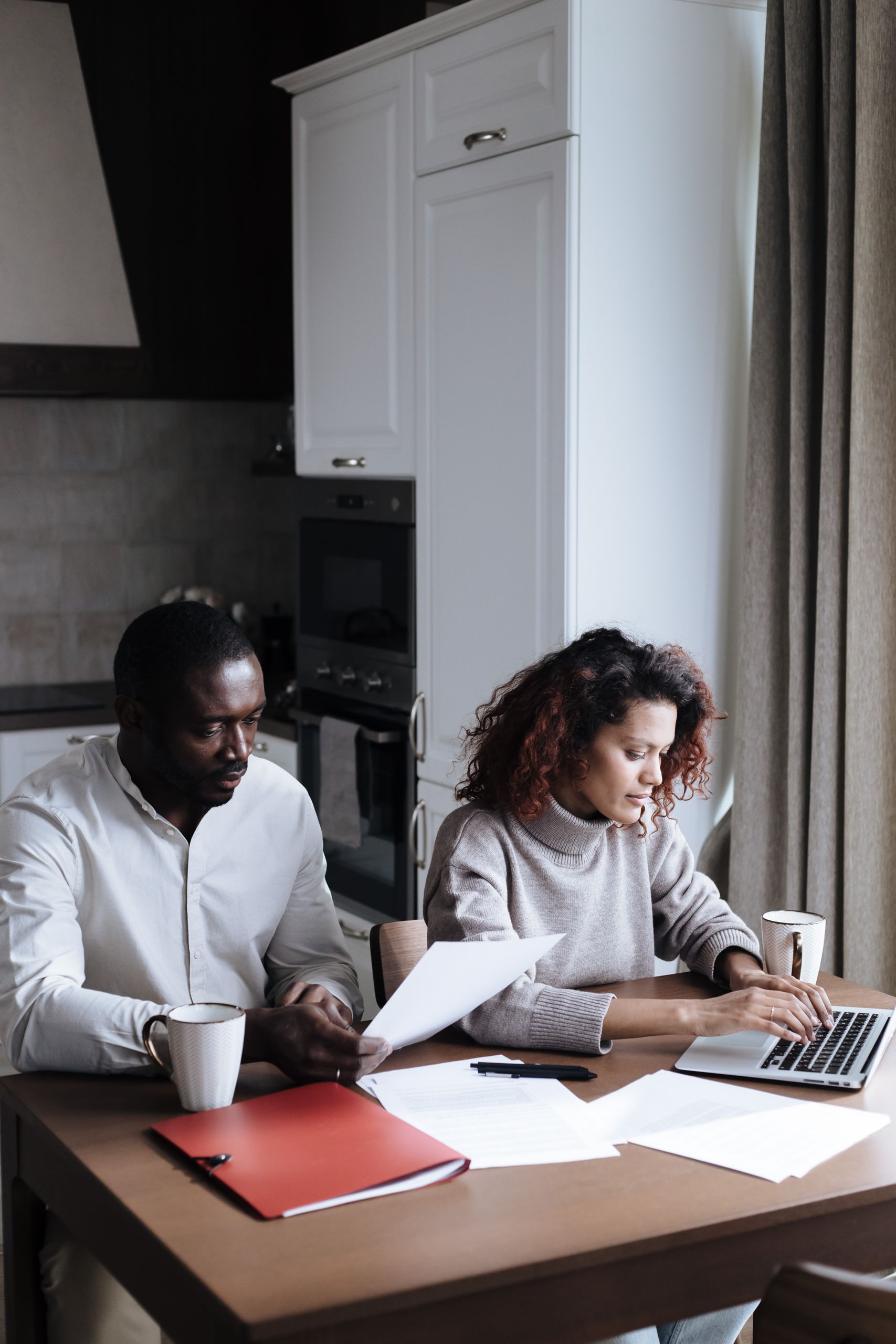 A couple reviewing documents together on a laptop in a modern kitchen setting.