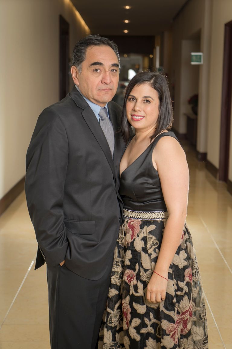A formally dressed couple poses indoors, highlighting elegance and grace at a special occasion.