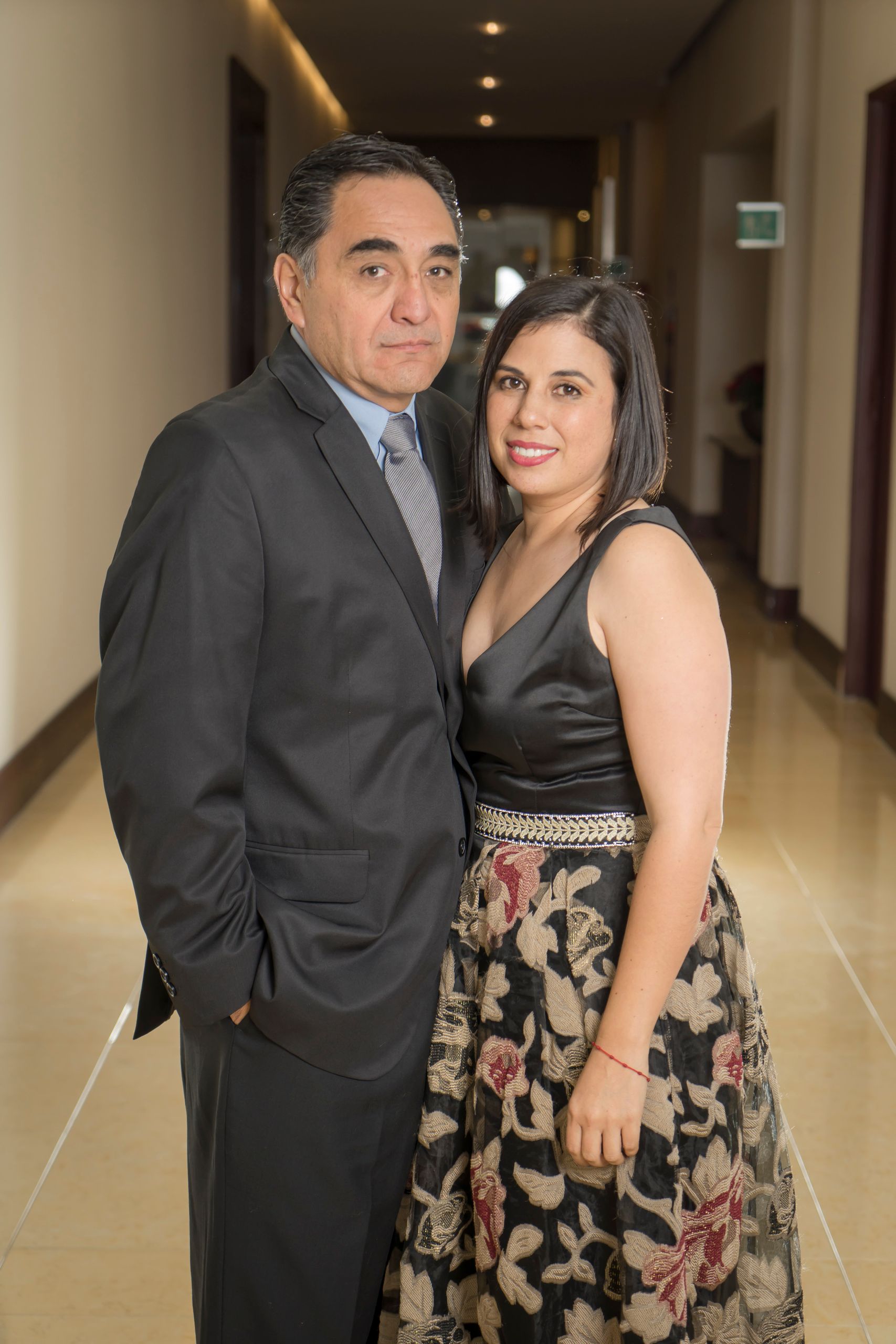 A formally dressed couple poses indoors, highlighting elegance and grace at a special occasion.