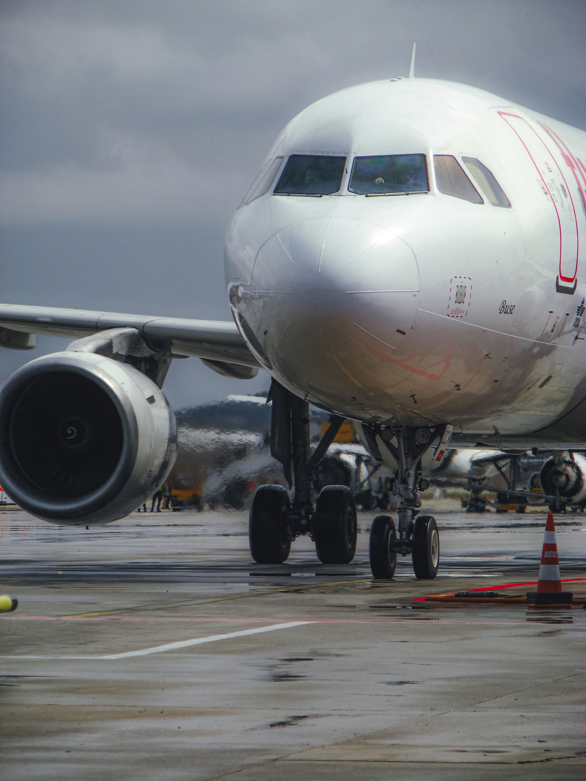 A large commercial airplane taxiing on a wet runway at an airport under cloudy skies.