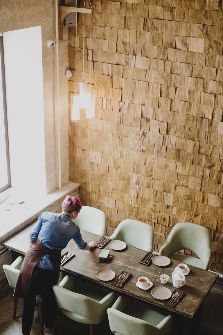 A person arranges a rustic dining table setting in a cozy restaurant interior.