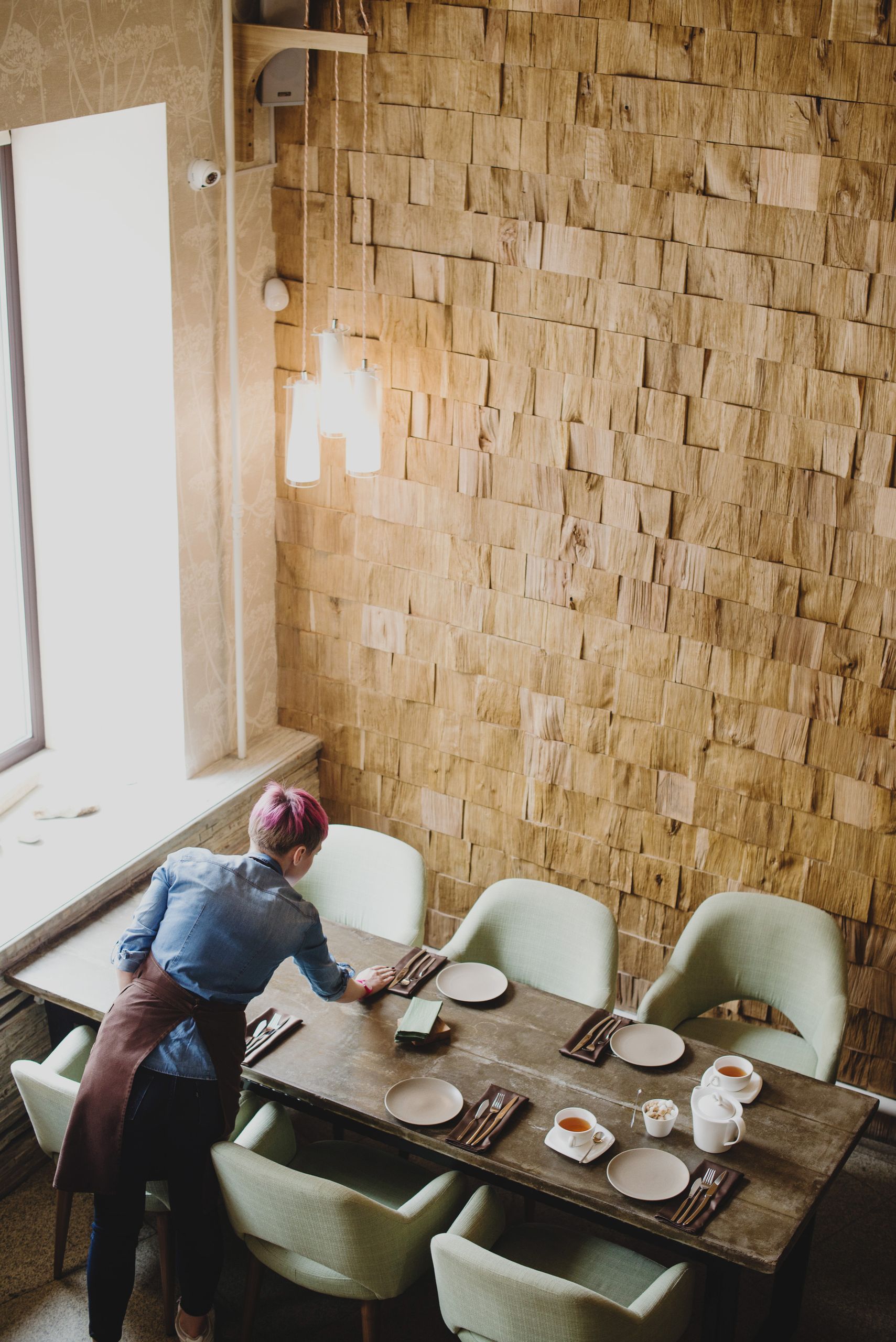 A person arranges a rustic dining table setting in a cozy restaurant interior.