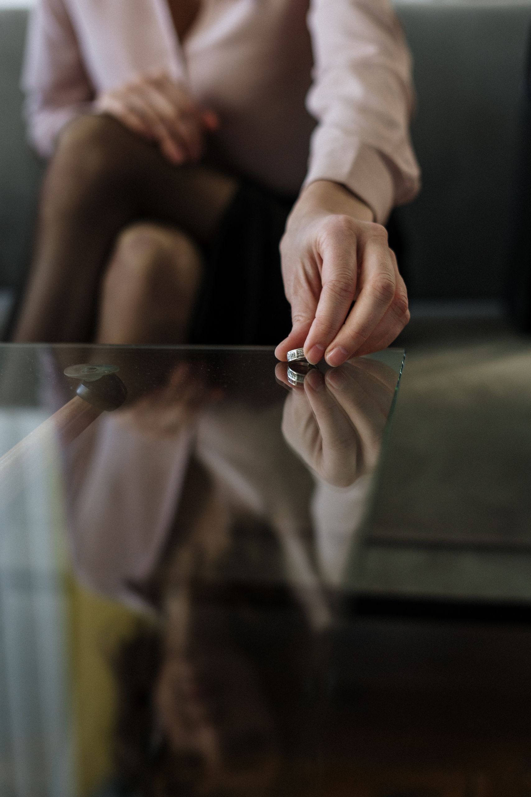 A person placing a wedding ring on a glass table, symbolizing separation or divorce.