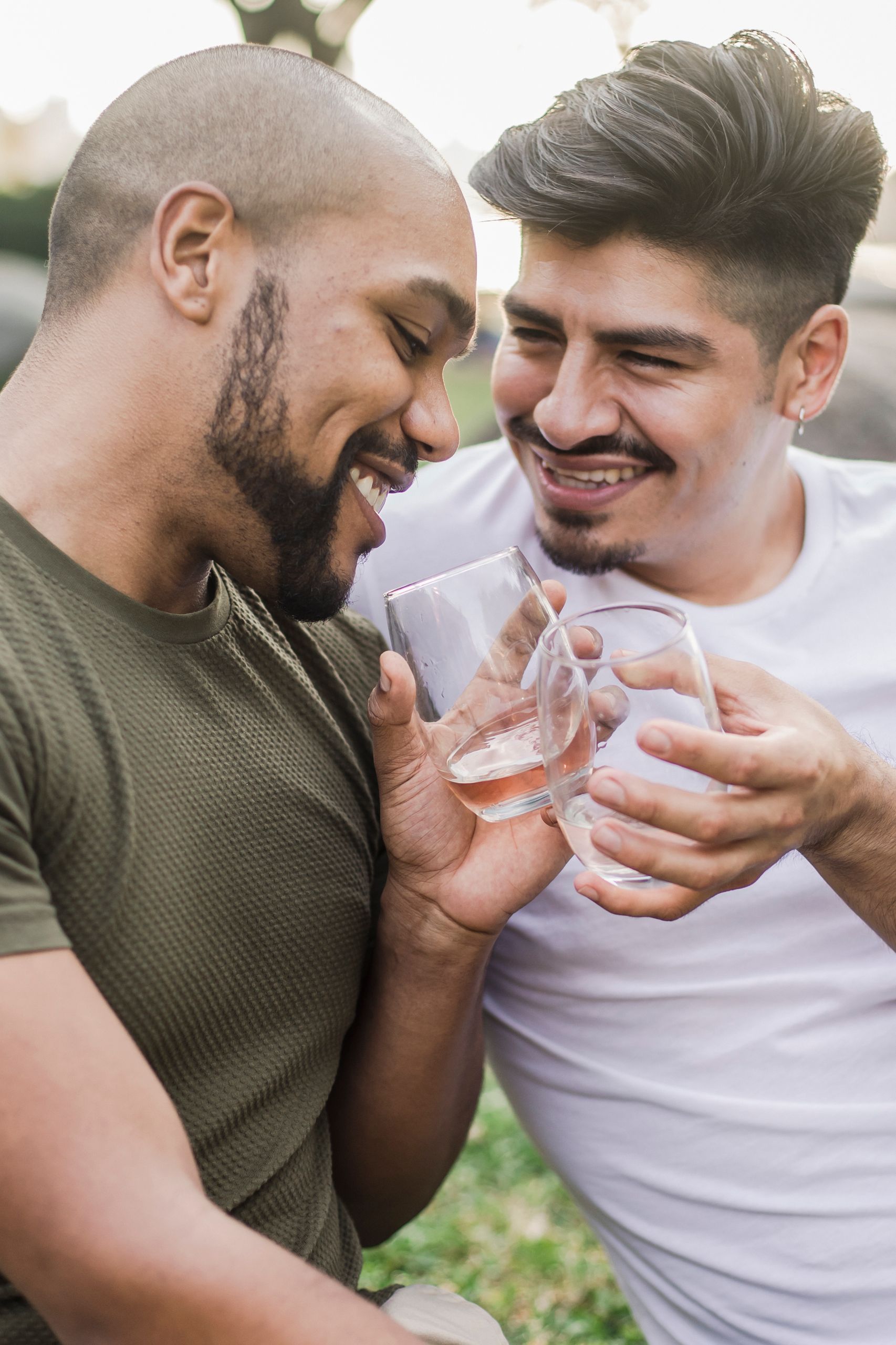 A smiling interracial gay couple sharing a joyful moment outdoors during the day, celebrating love and togetherness.