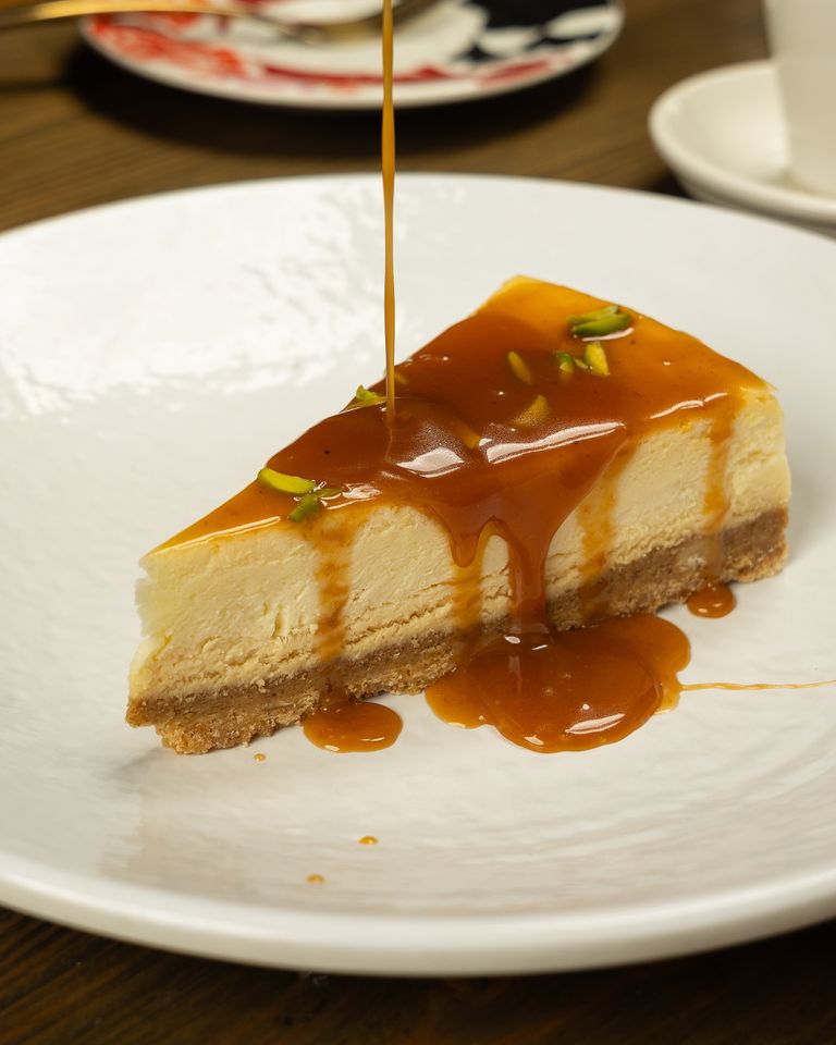A tempting slice of cheesecake topped with a rich caramel drizzle and garnished with pistachios.