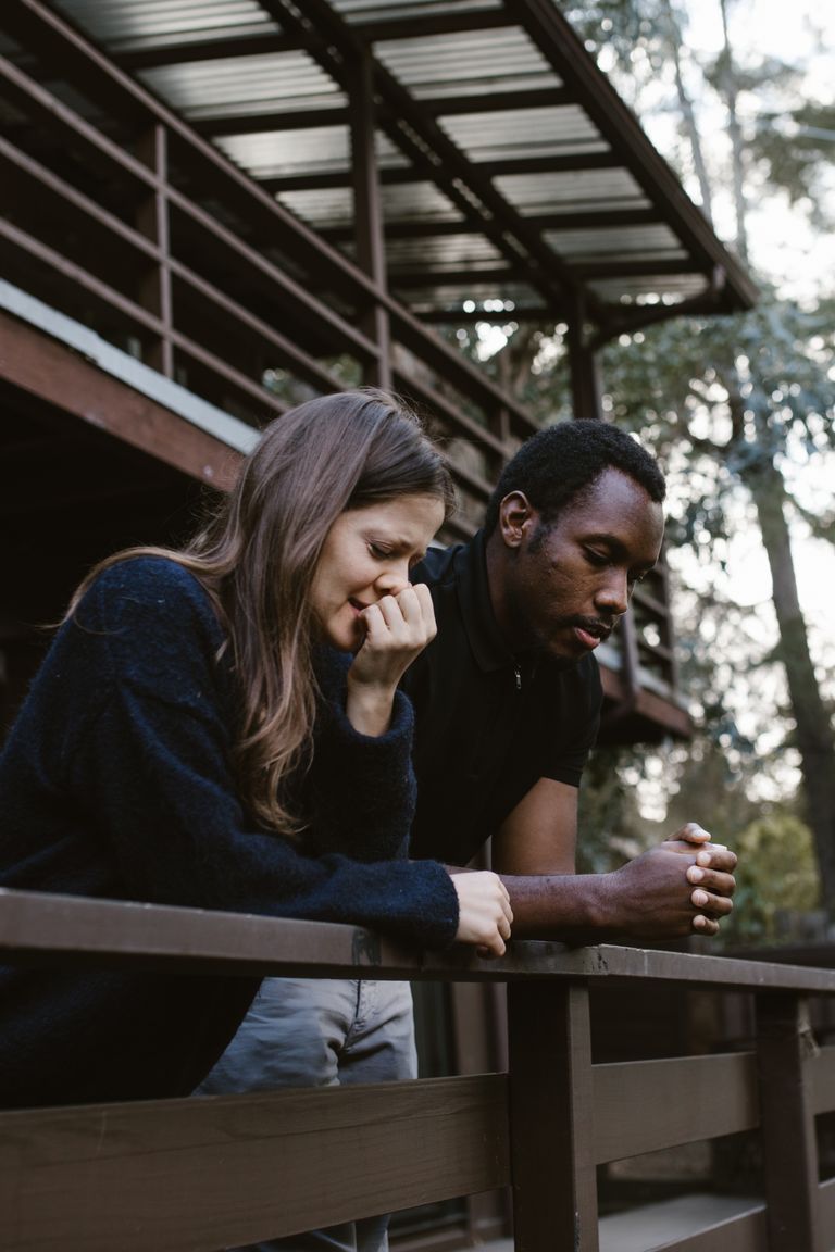 A thoughtful and emotional moment captures a couple reflecting on a balcony, embraced by nature.