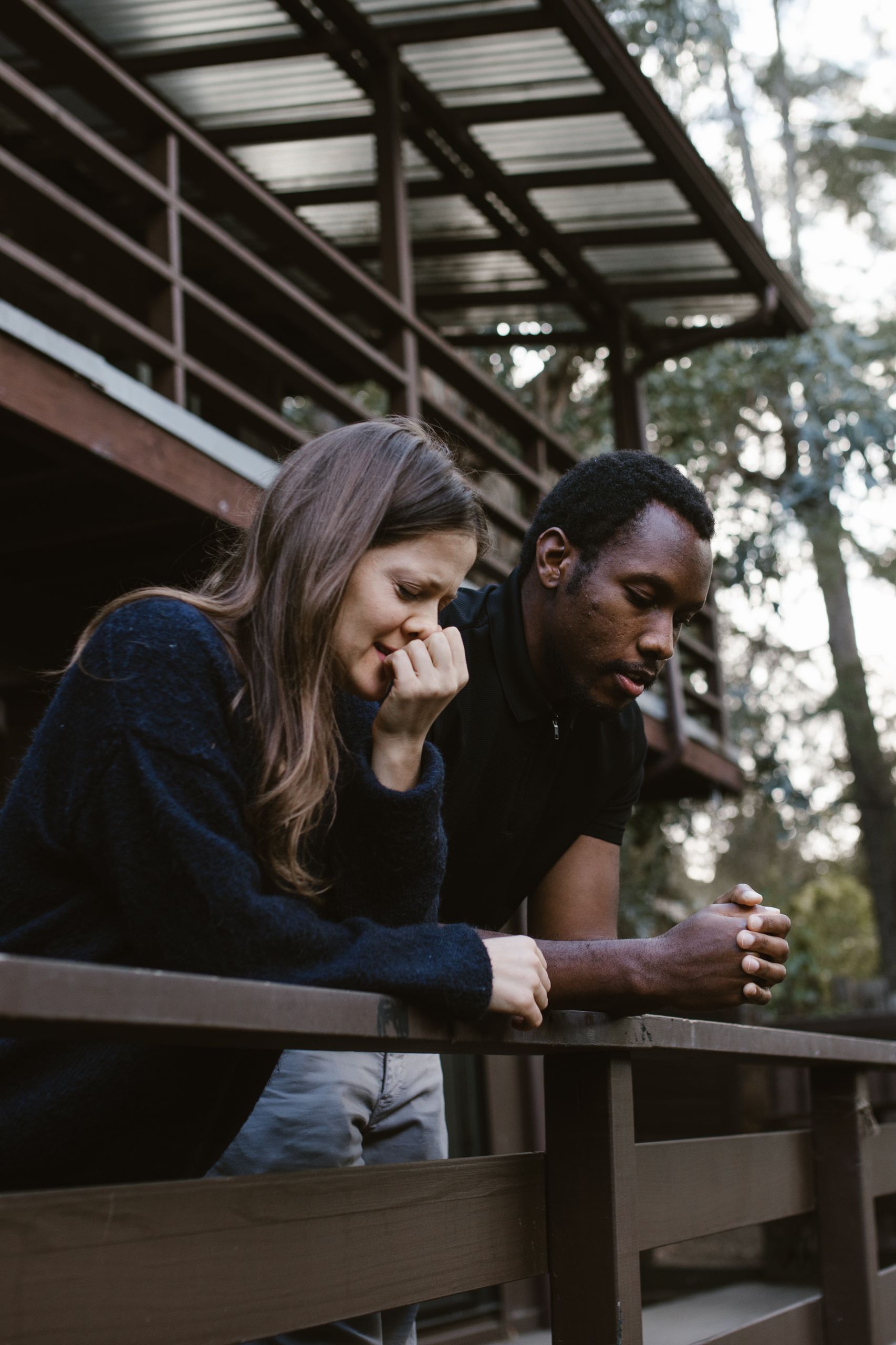 A thoughtful and emotional moment captures a couple reflecting on a balcony, embraced by nature.