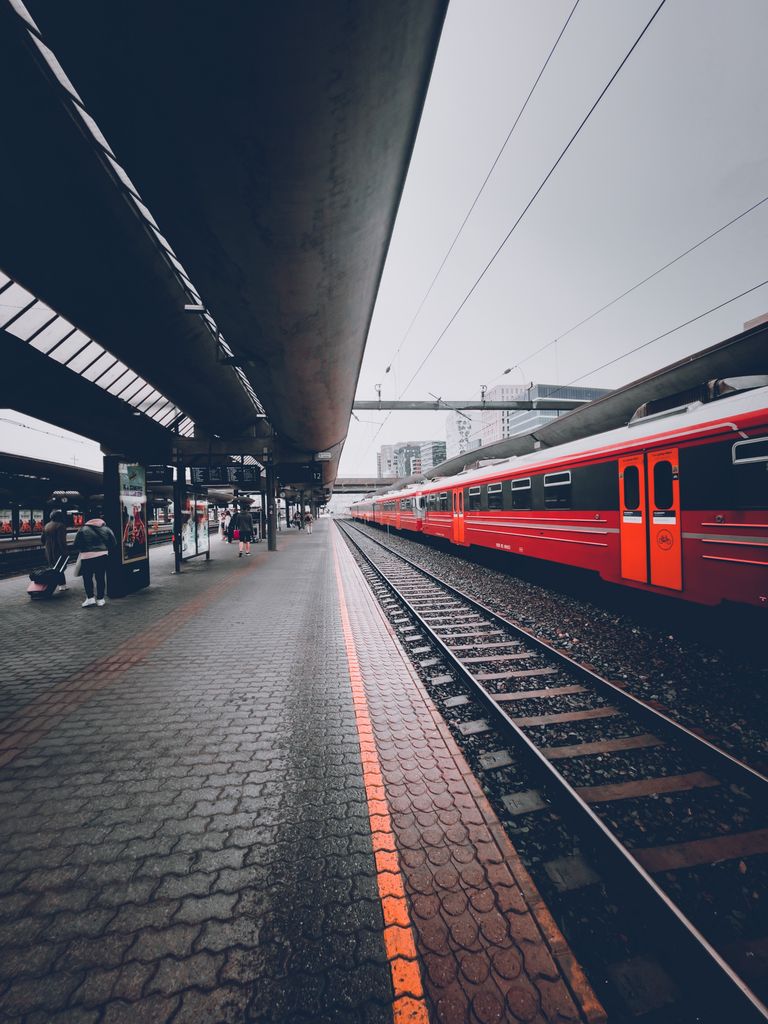 A vibrant red train at a bustling railway station under an overcast sky.