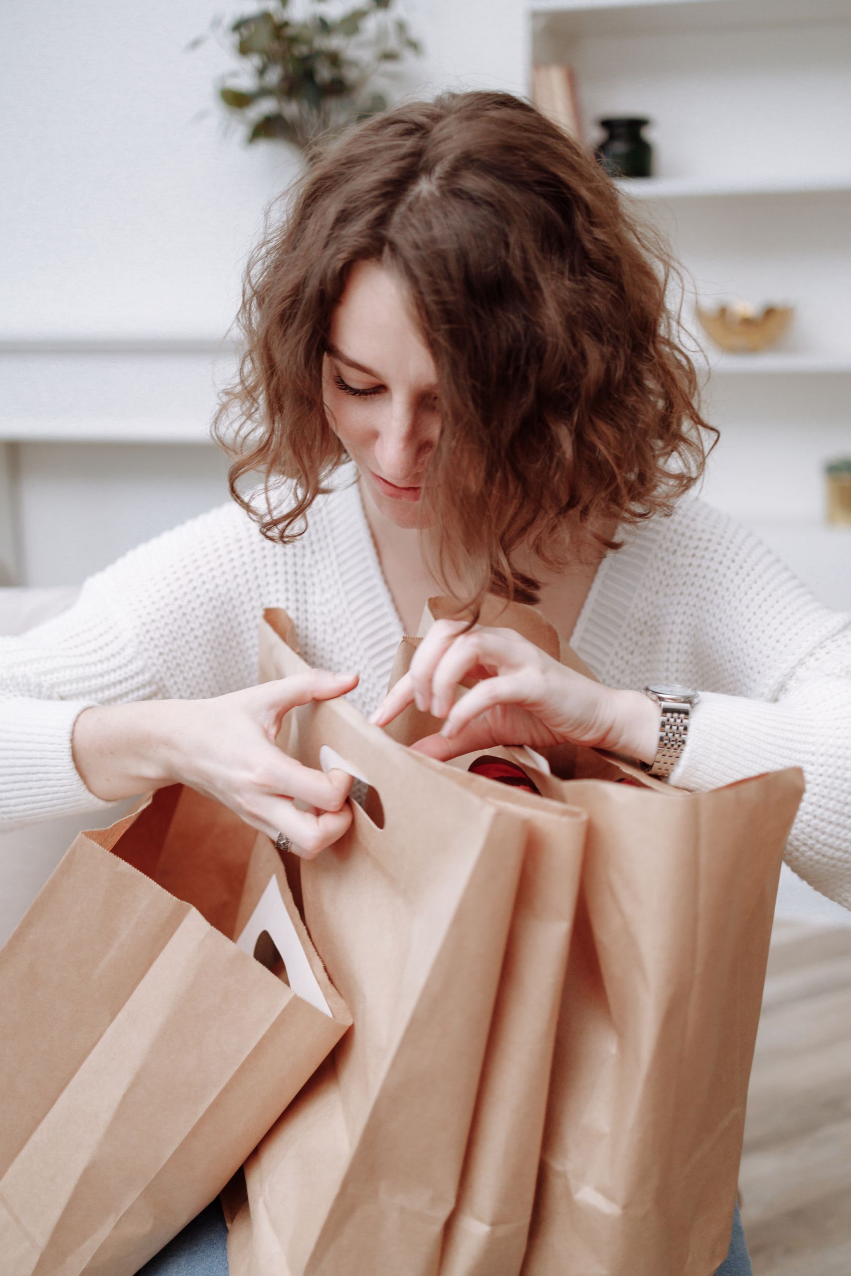 A woman in a white sweater looks into shopping bags indoors, creating a cozy, minimalist vibe.