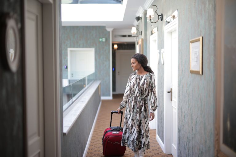 A woman walks with luggage through a stylish hotel corridor, embodying travel elegance.