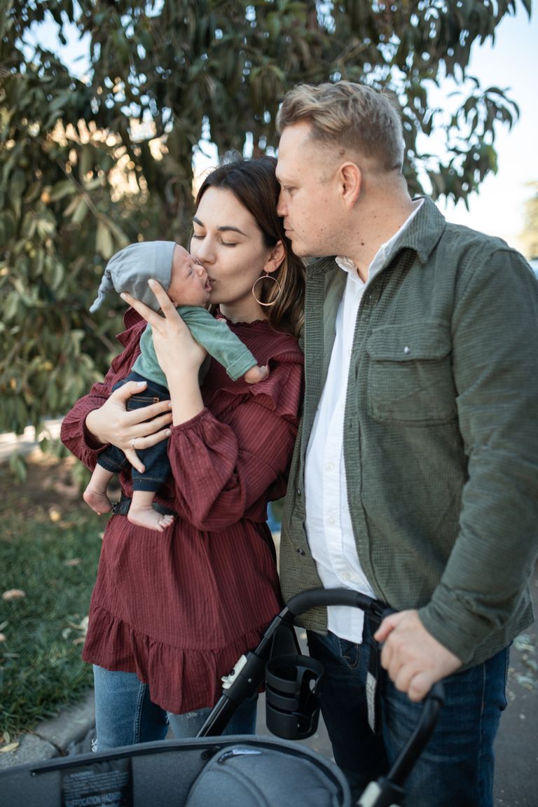 A young couple shares a tender moment with their newborn in a park setting.