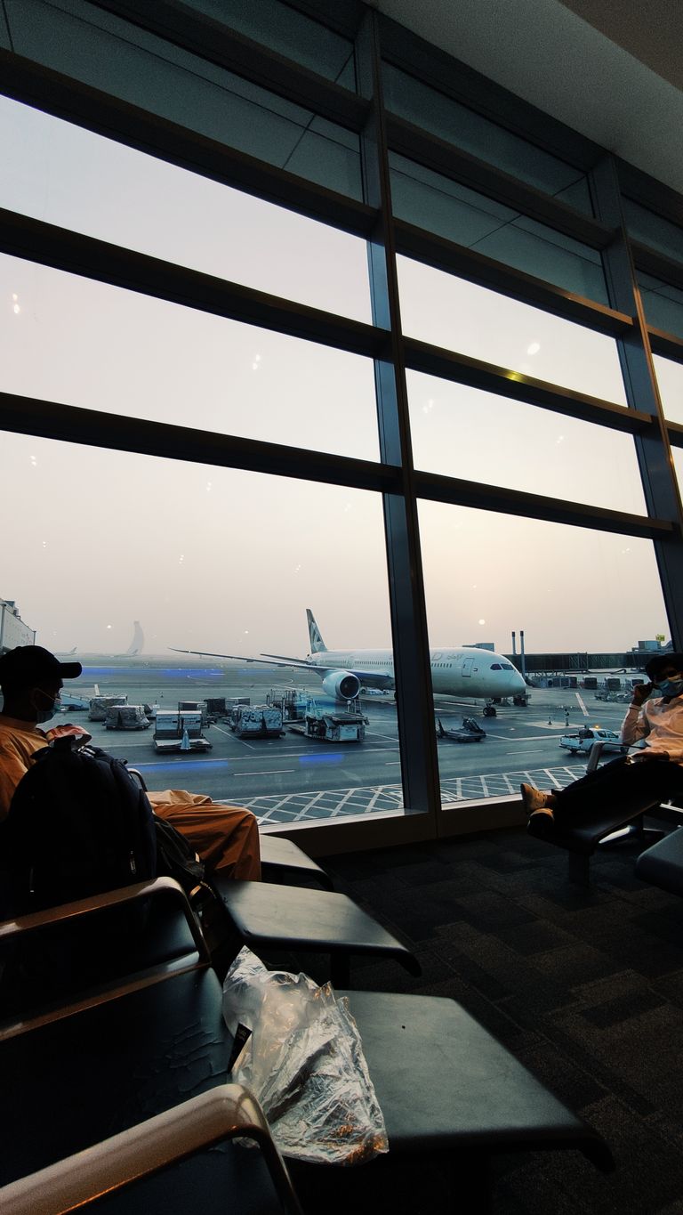 Airplane on tarmac viewed through windows in Abu Dhabi's airport lounge at sunset.