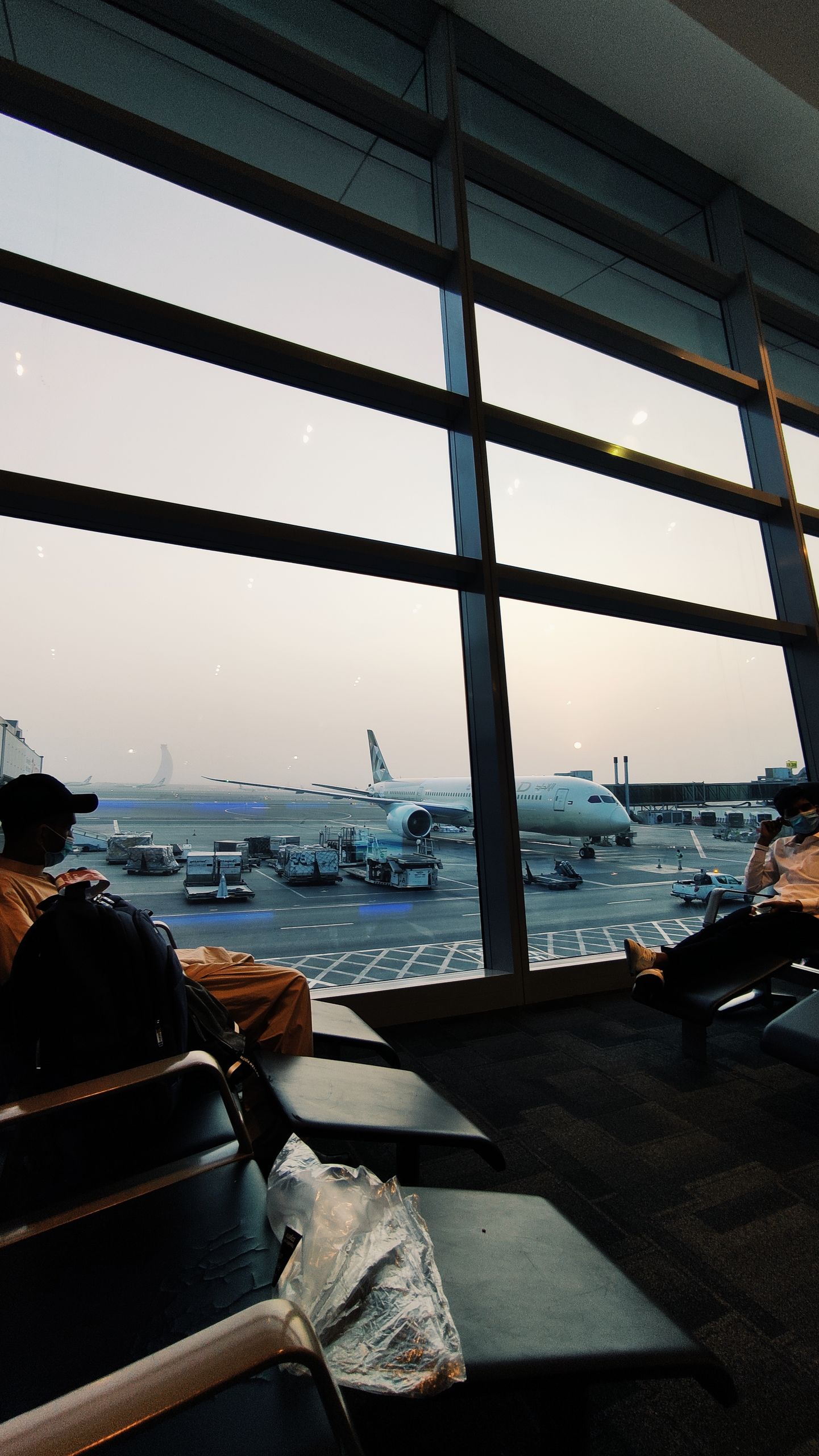 Airplane on tarmac viewed through windows in Abu Dhabi's airport lounge at sunset.