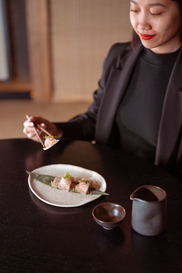 Asian woman dining with chopsticks, savoring delicious sushi indoors.