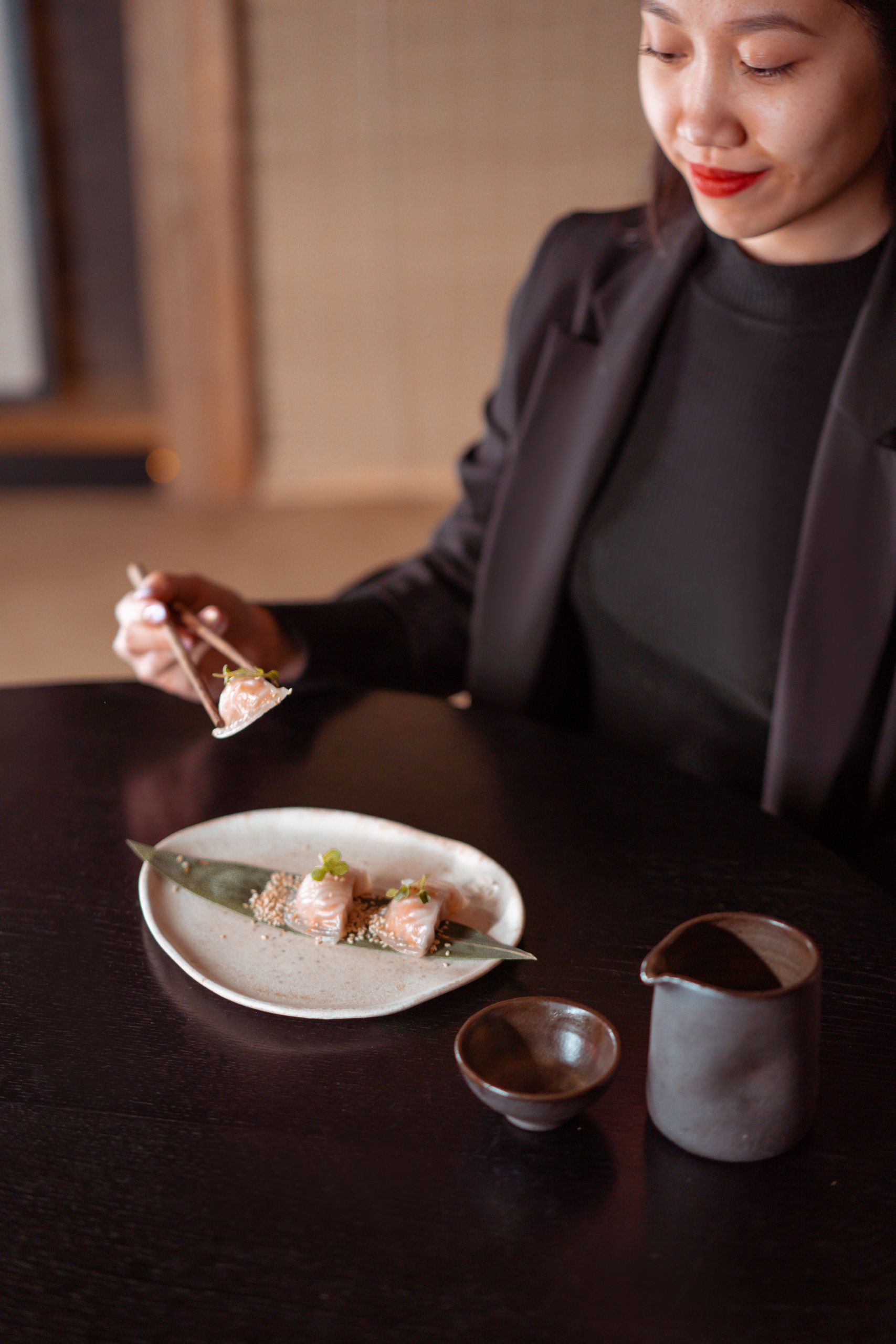 Asian woman dining with chopsticks, savoring delicious sushi indoors.