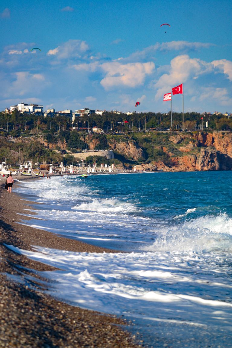 Beautiful beach scene with waves and Turkish flags waving on a sunny day.