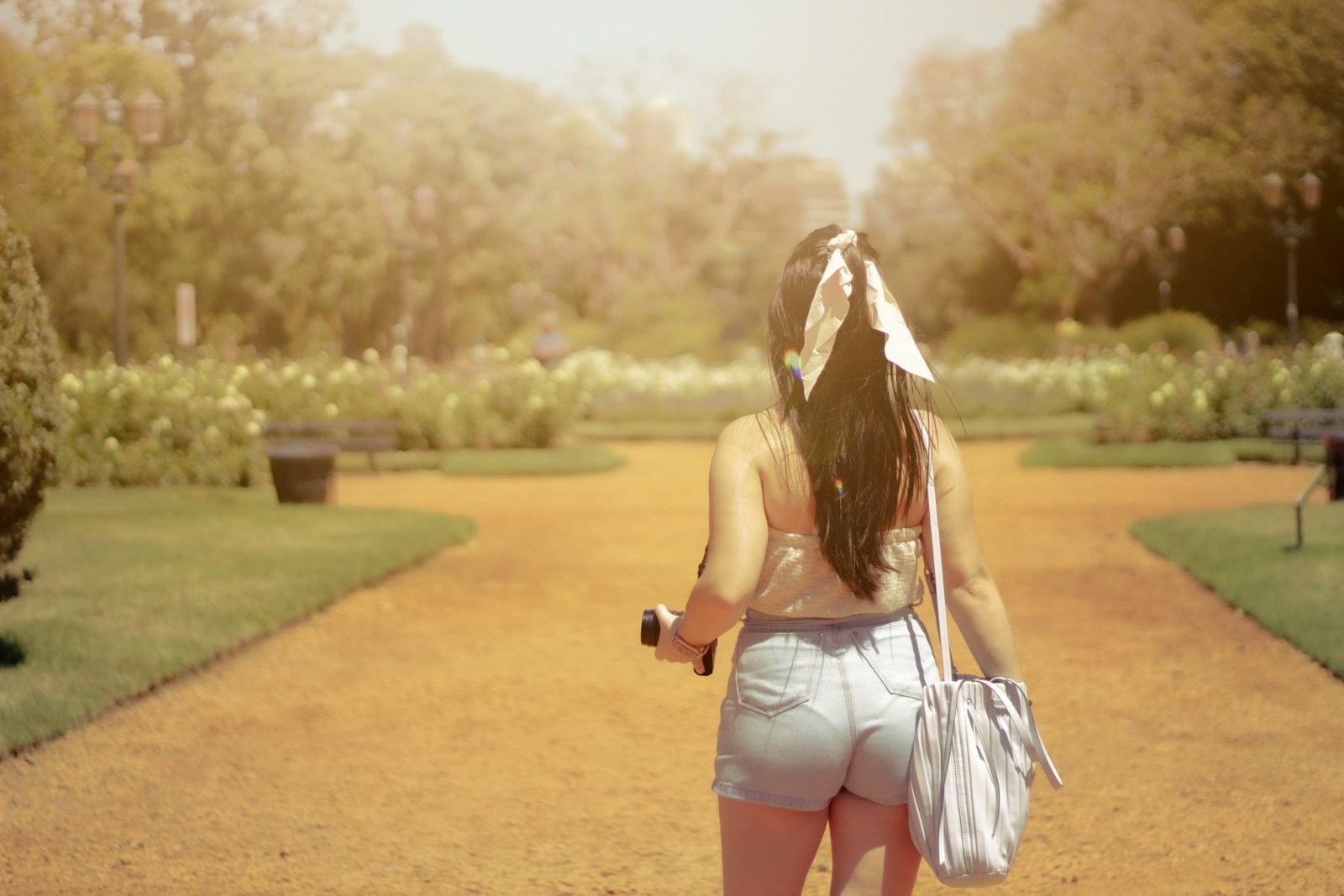 a woman walking down a dirt road carrying a purse