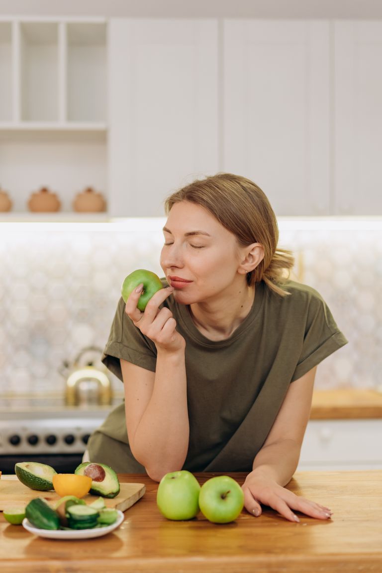 Caucasian woman savoring green apples in a cozy kitchen setting, embodying a healthy lifestyle.