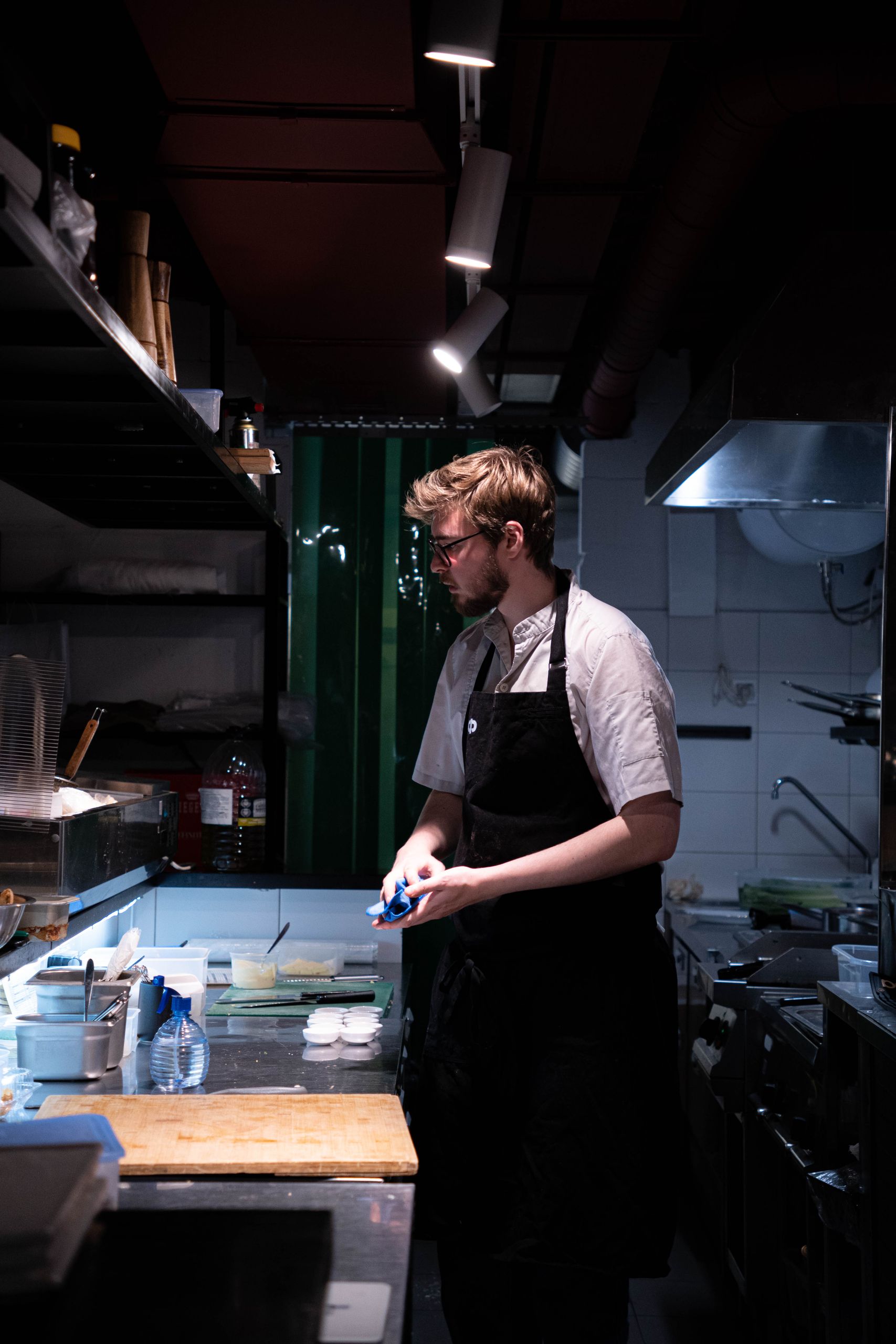 Chef working on meal preparation in a well-equipped kitchen with focused lighting.