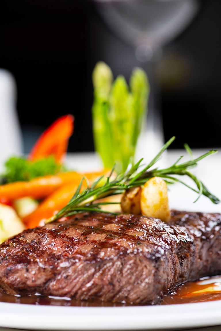Close-up of a juicy grilled steak with colorful vegetables on a plate, perfect for a gourmet meal.