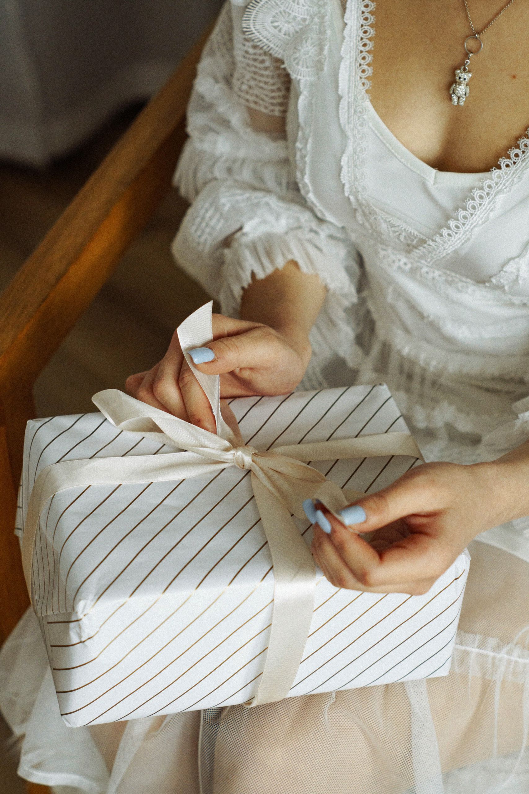 Close-up of a woman in a lace dress skillfully untying a gift ribbon.