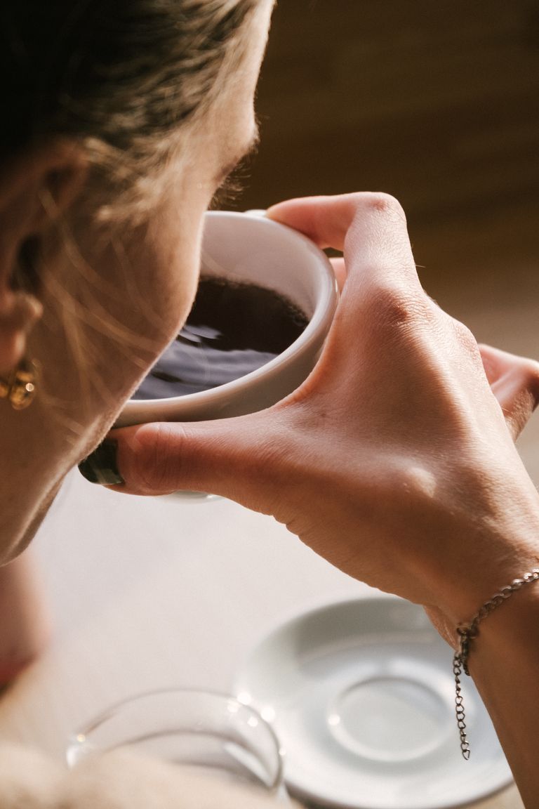 Close up of a woman savoring a coffee indoors in soft morning light.
