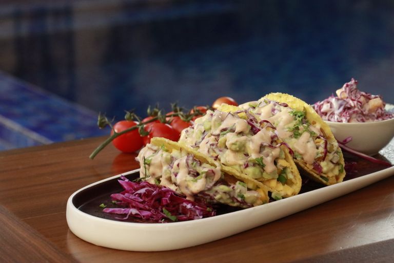 Close-up of appetizing tacos with creamy vegetable filling on a ceramic plate by the pool.