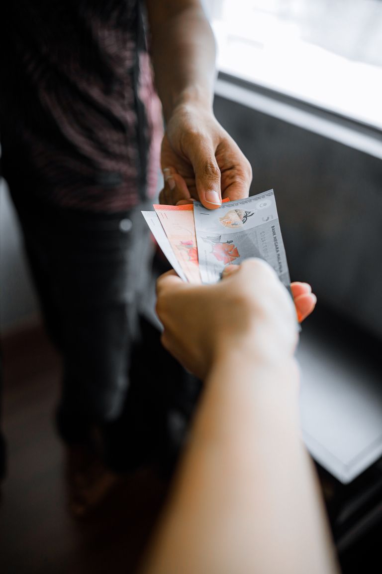 Close-up of hands exchanging Malaysian Ringgit notes indoors.