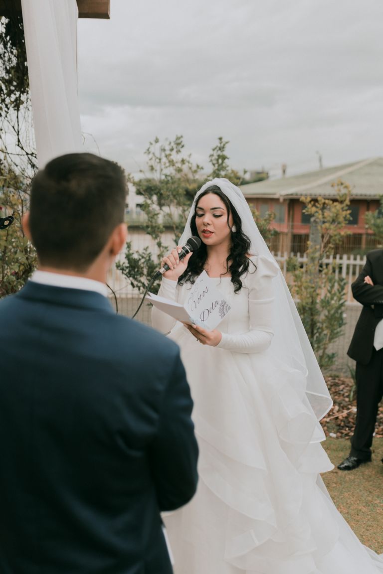 Elegant wedding ceremony featuring bride with microphone and groom outdoors.