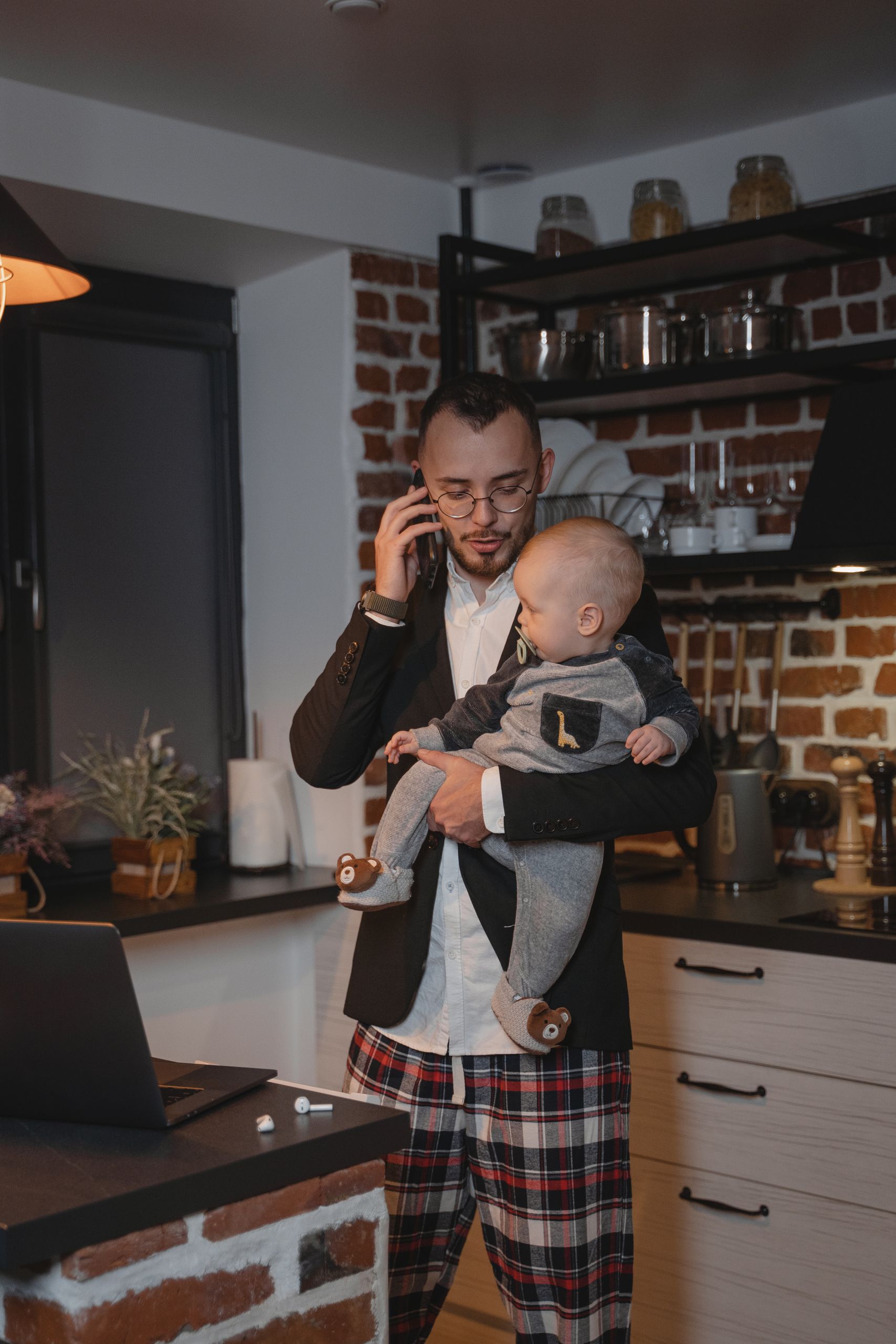 Father working from home office while holding baby and talking on cellphone, illustrating the balance of family and work.