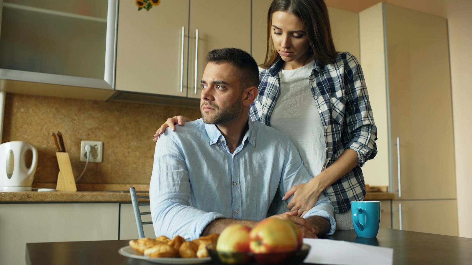 Woman comforts man at kitchen table with food