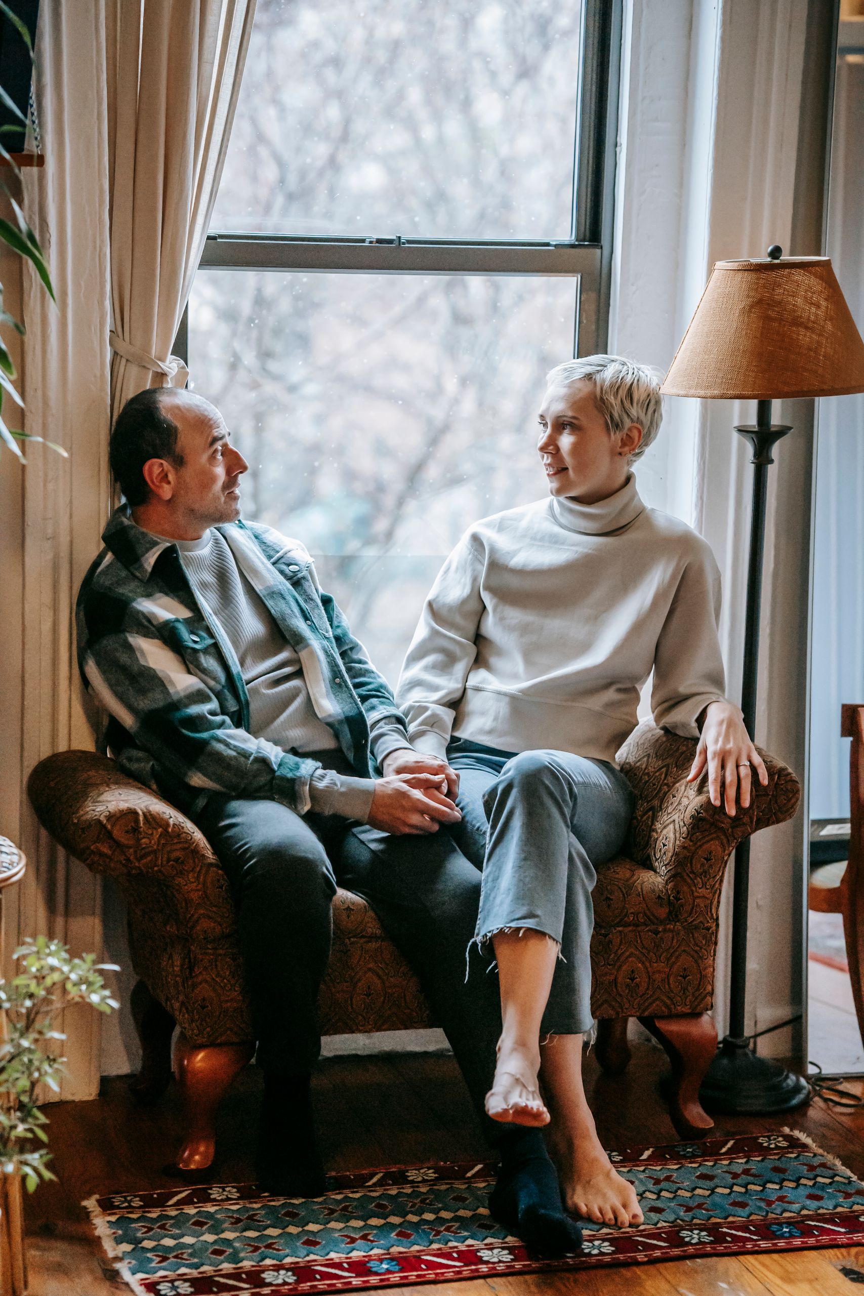 Full body of cheerful middle aged couple relaxing on couch while speaking in cozy lounge