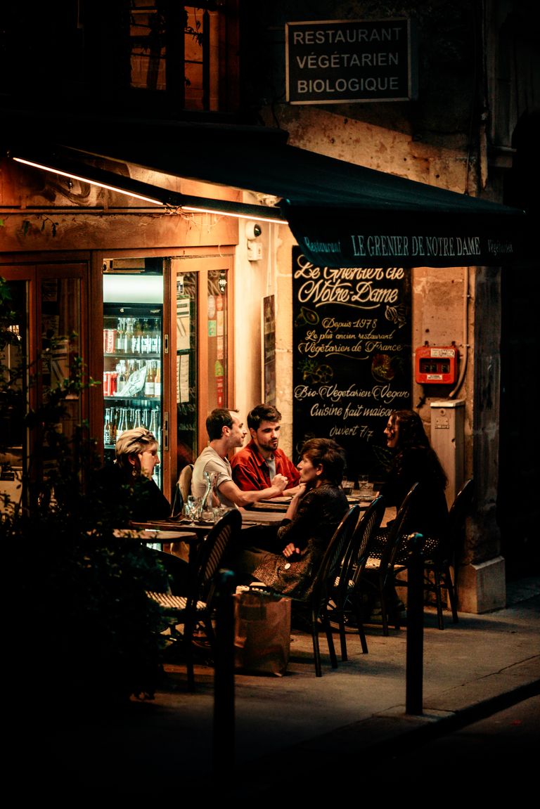 Group dining outdoors at a Parisian restaurant, warm ambiance, night.