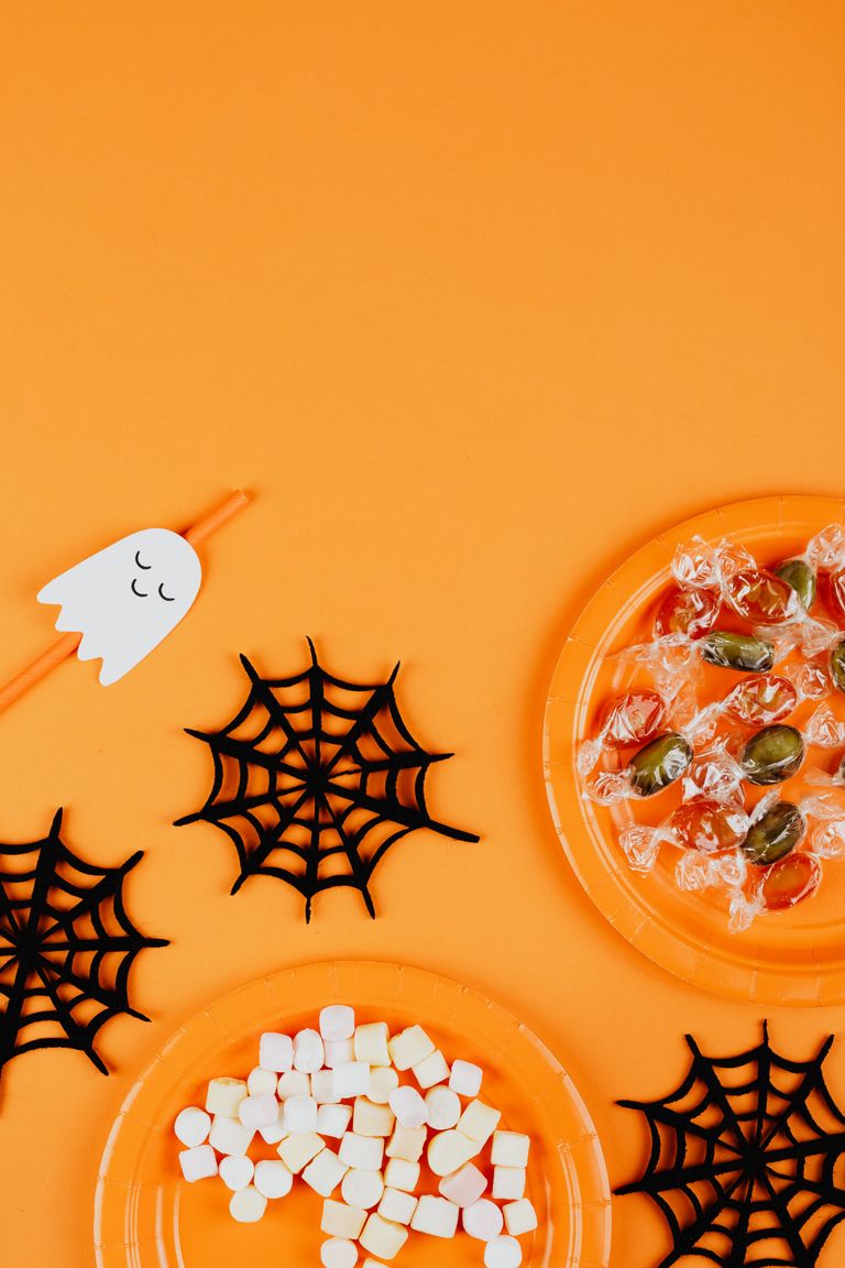 Halloween-themed flat lay featuring candies and decorations on an orange background.