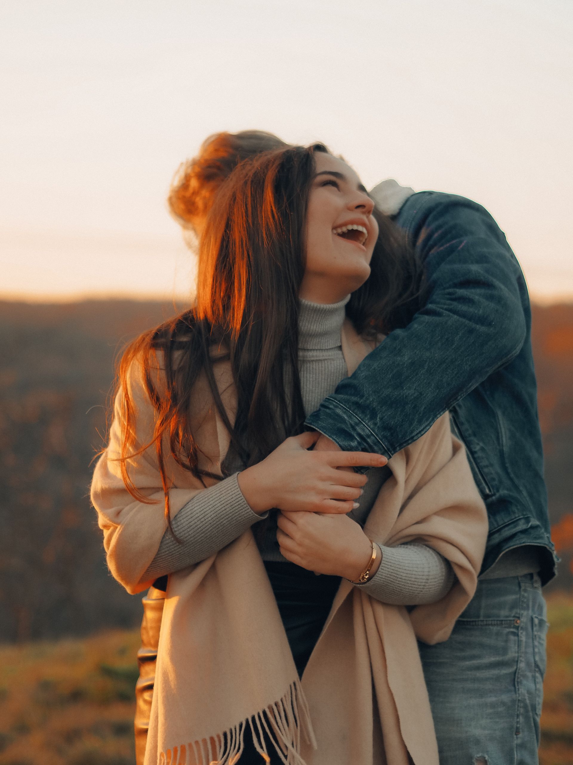 Happy couple embracing outdoors during sunset, sharing a romantic moment filled with laughter.
