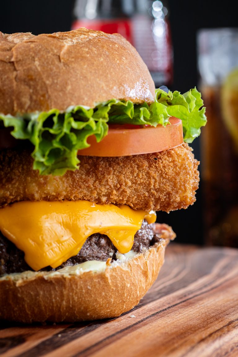 Mouthwatering burger with cheese, lettuce, tomato, and fried onion on a wooden board.