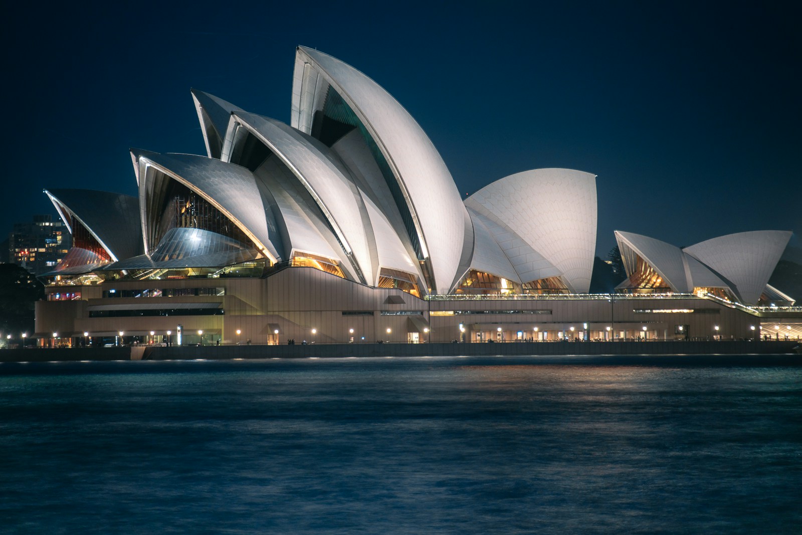 The sydney opera house illuminated at night over water