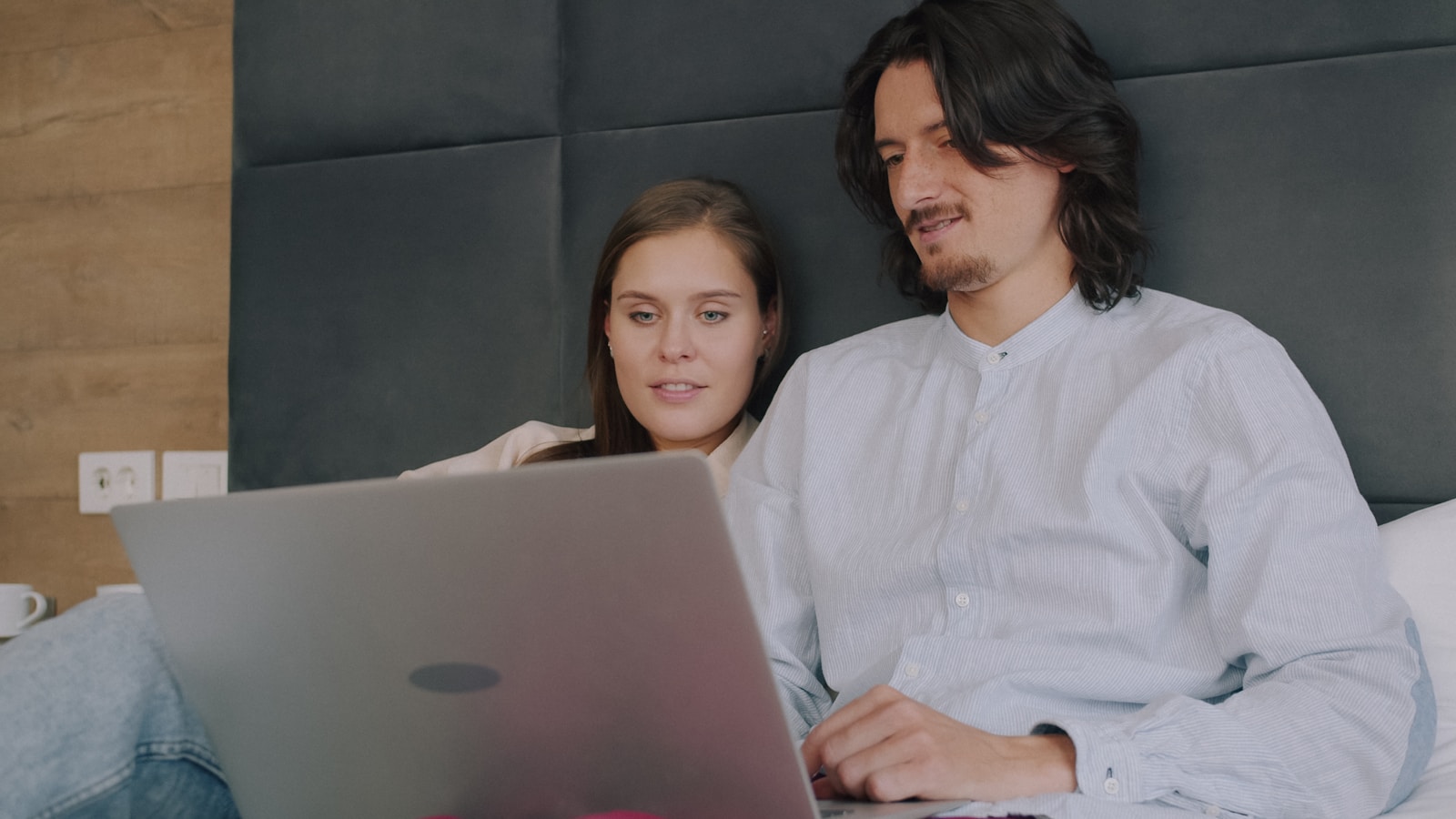 A man and a woman using a laptop while sitting on a bed