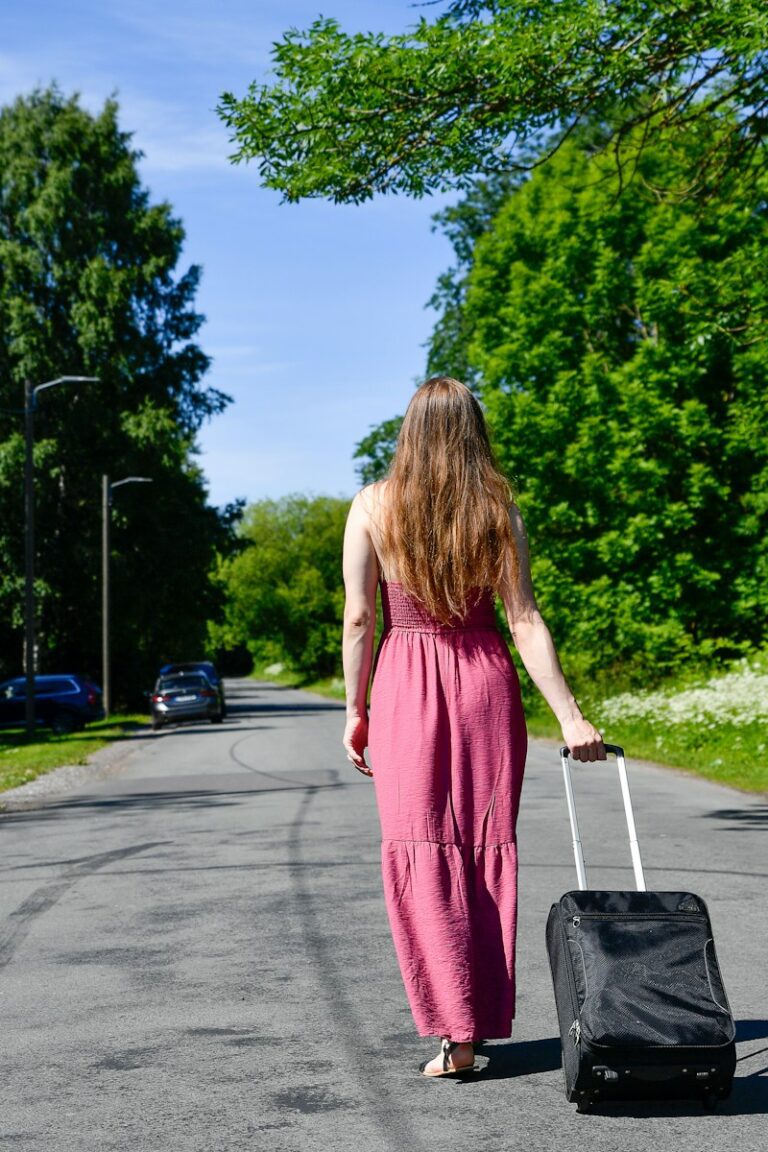 A woman walks with a suitcase on a tree-lined road