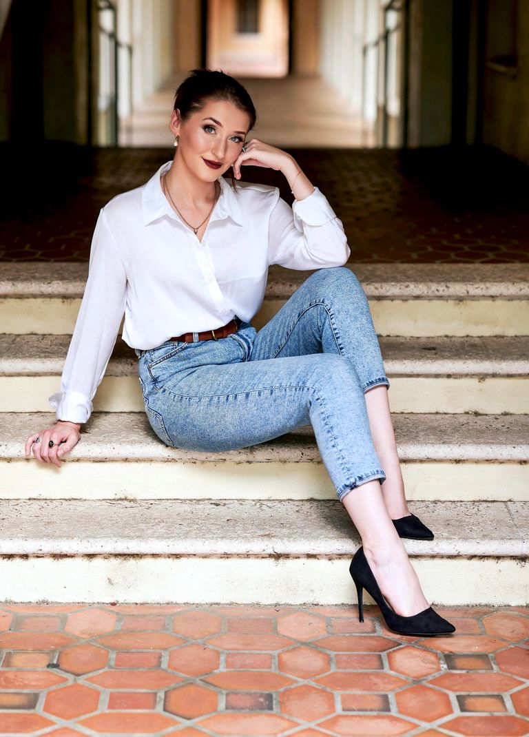 Stylish young woman in jeans and a white shirt poses confidently while sitting on stairs.