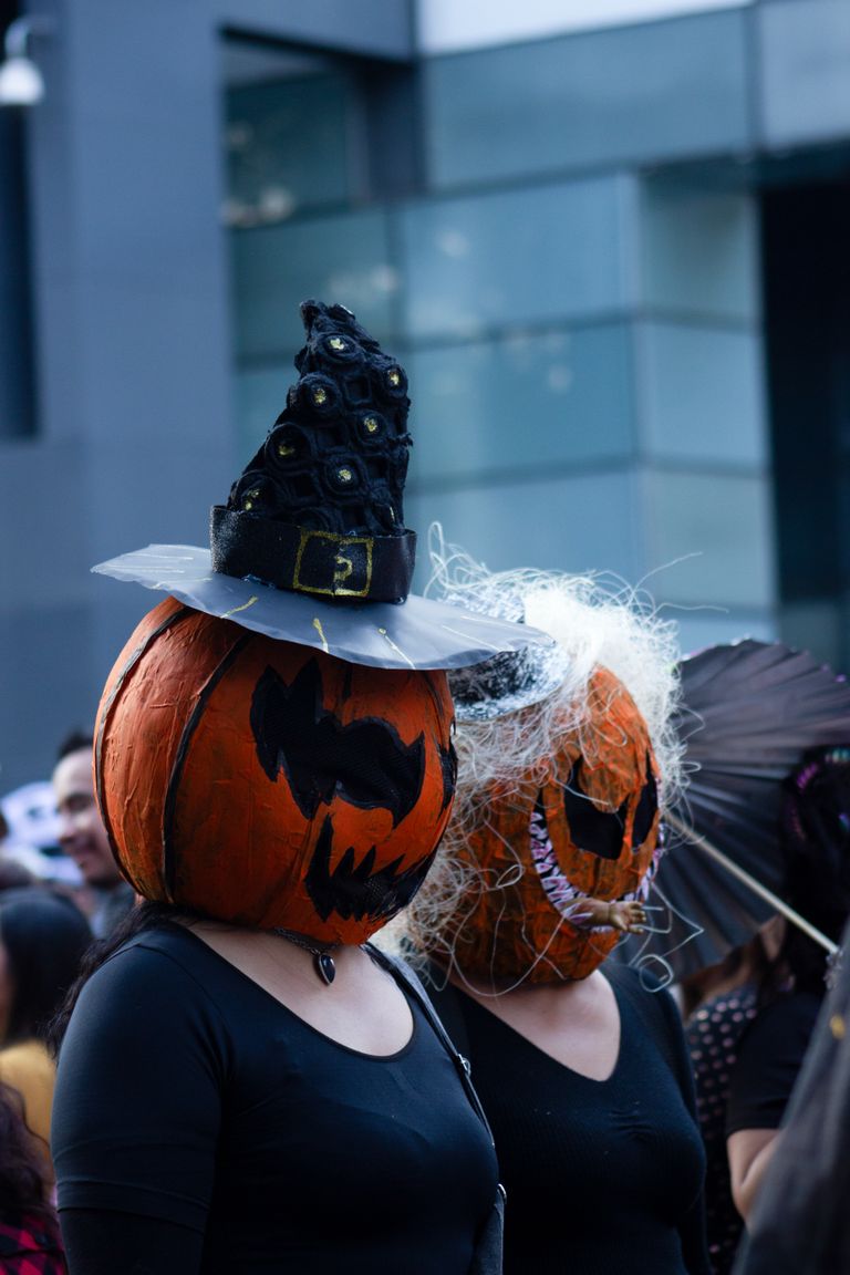 Two people wearing creative pumpkin head costumes on a busy city street during Halloween.