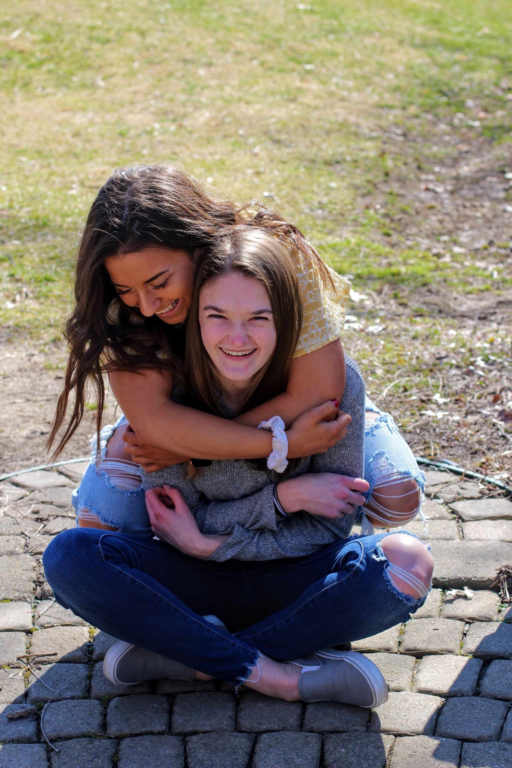 Two young women sharing a joyful hug outdoors in the sun.