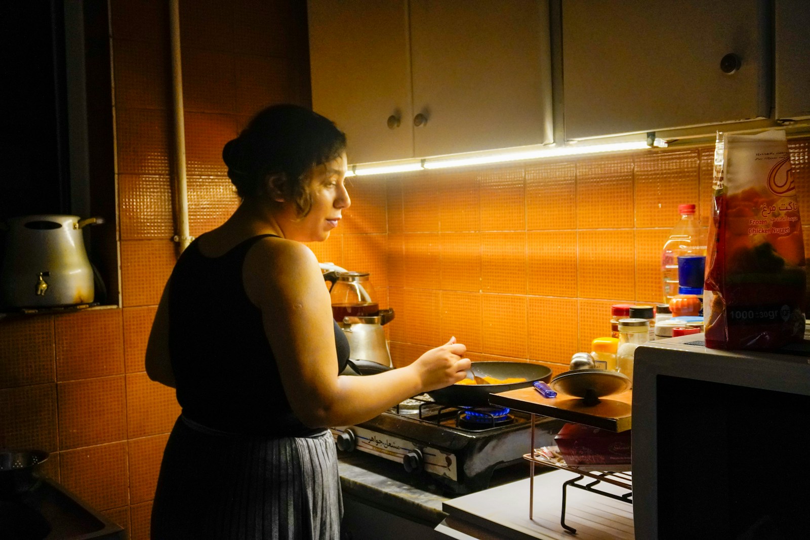 A woman cooks food in a small kitchen