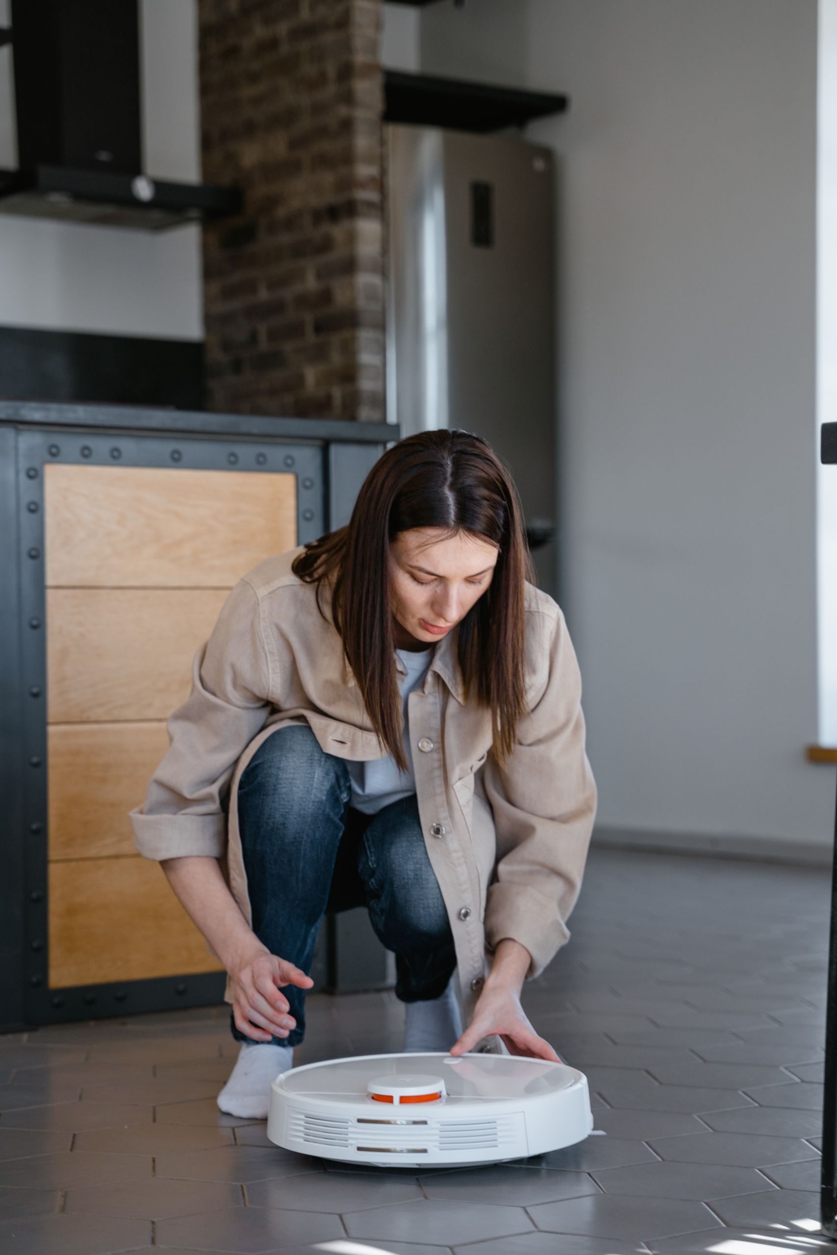 Woman adjusting a robotic vacuum cleaner on a tiled floor indoors.